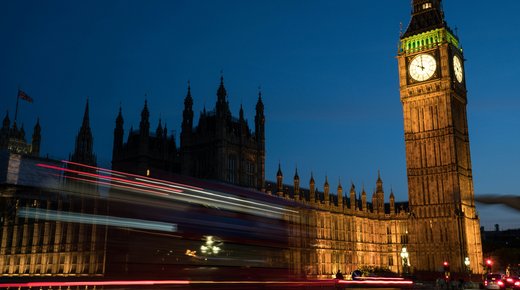 A shot of Big Ben at night time with a blurred double decker red bus moving past