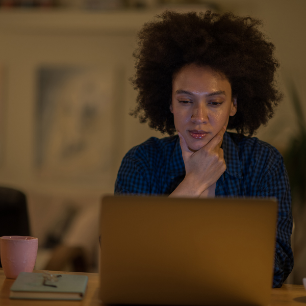 A woman sits at a table looking seriously at her laptop.